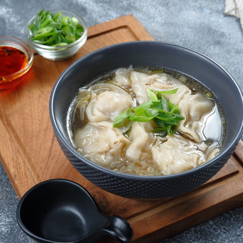 A bowl of Great Wall Restaurant's wonton soup with green onions, chili oil, and a spoon.