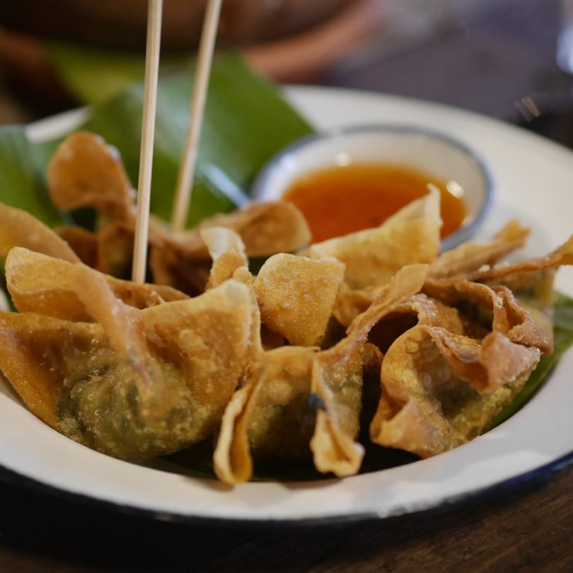 Crispy fried wontons with a side of sweet chili dipping sauce on a white plate with green leaves.
