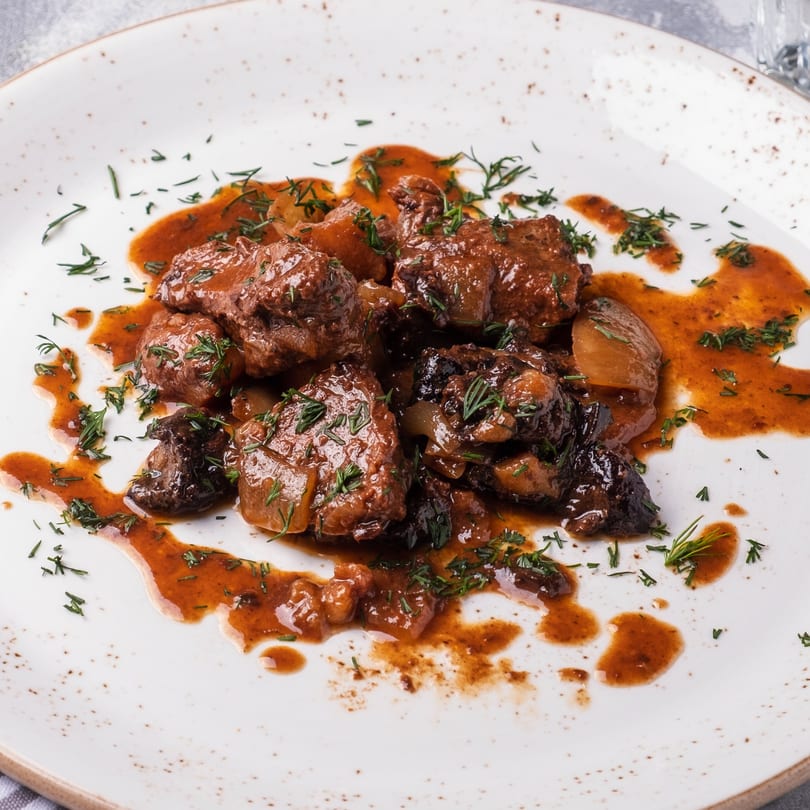 Braised beef with mushrooms and onions in a rich brown sauce, garnished with fresh dill.