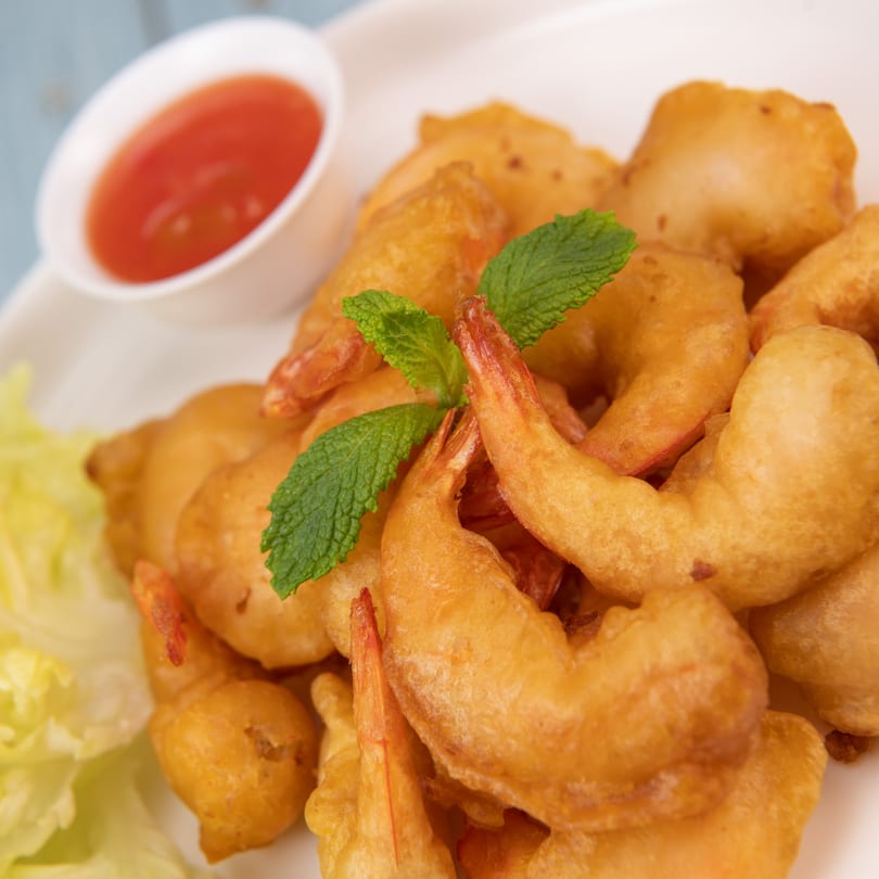 Golden-fried shrimp tempura with a side of sweet chili sauce and a mint garnish.