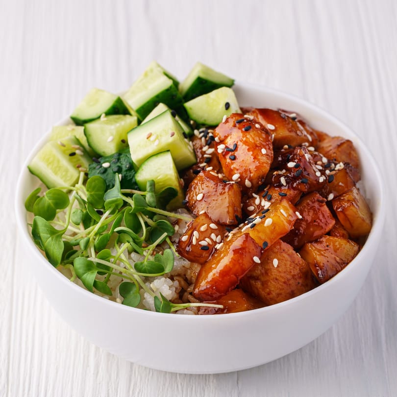A Chinese dish with glazed chicken, cucumbers, and microgreens in a white bowl.