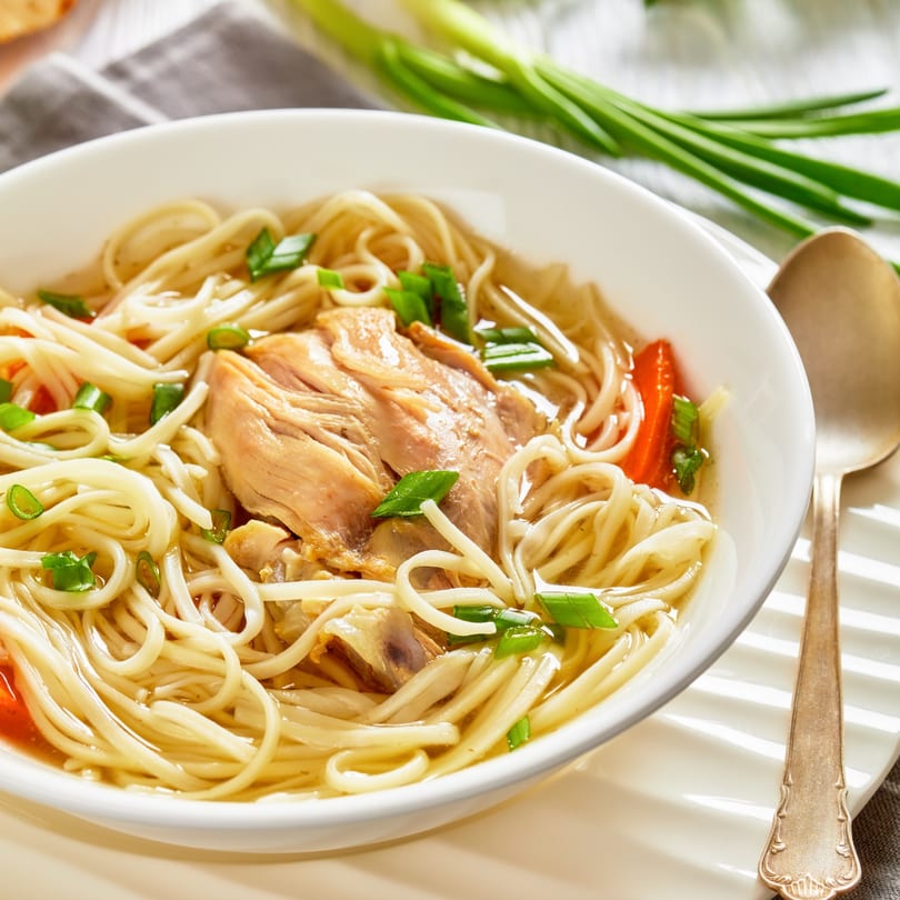 Close-up of a white bowl filled with Great Wall Restaurant's chicken noodle soup, garnished with scallions.
